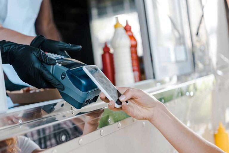 A person is using a mobile phone to pay for food at a food truck using Vendor Management Systems.