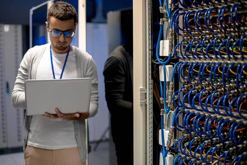 A man using a laptop in a server room with managed IT services in Boston.