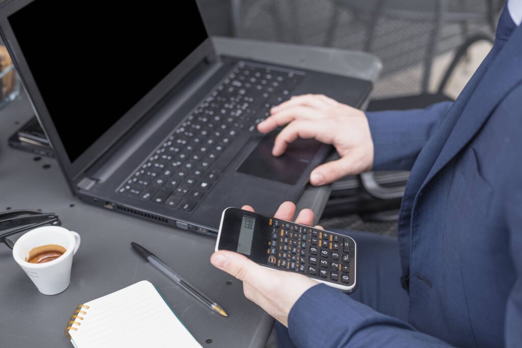 A man in a suit is using a calculator on a laptop to provide Managed IT Services in Worcester.