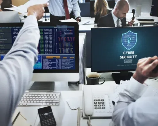 A group of financial professionals working in an office with a computer screen showing a network security logo.