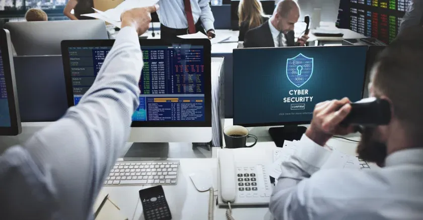 A group of financial professionals working in an office with a computer screen showing a network security logo.