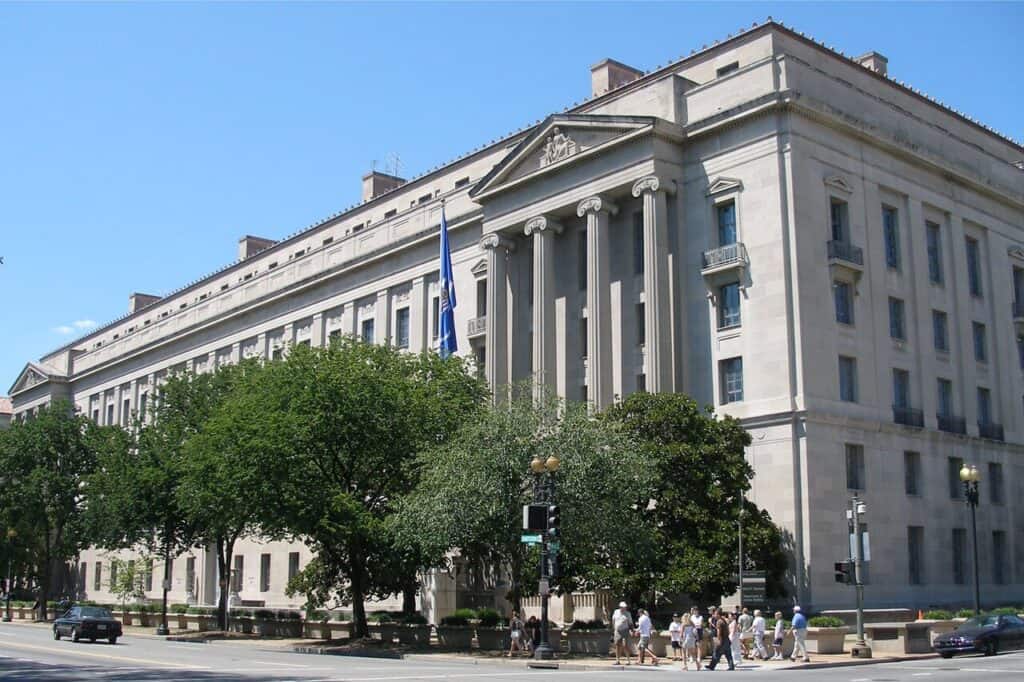 A large, classical-style government building with columns and a flag stands surrounded by trees and people walking on the sidewalk, symbolizing unity in efforts to Take Down Lockbit.