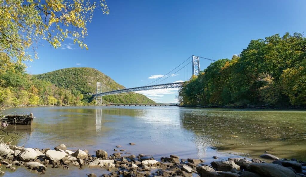 Suspension bridge spanning a river with lush green hills under a clear blue sky, near the managed IT services in Rockland.