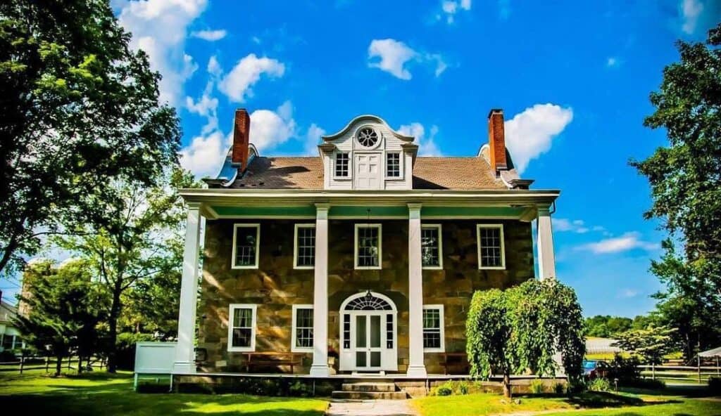 A classic two-story colonial house with a centered front door and symmetrical windows, surrounded by lush green trees under a blue sky managed IT services Lincoln, RI.