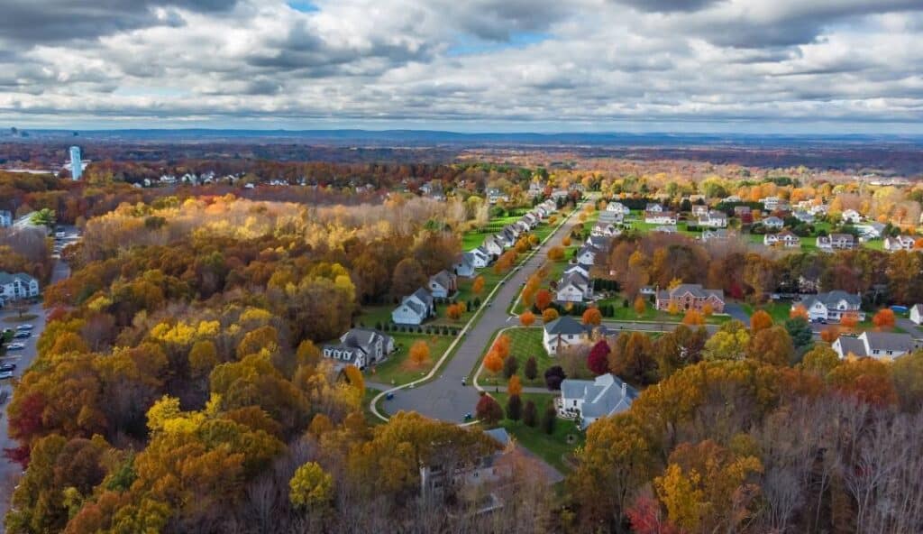 Aerial view of a suburban neighborhood with rows of houses surrounded by colorful autumn trees under a cloudy sky, showcasing the area's managed IT services in Manchester.