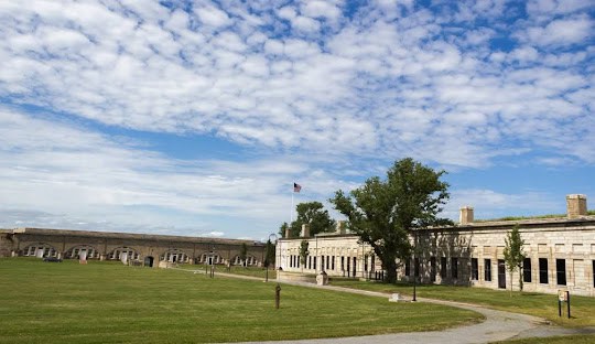 A historic stone fort in Jamestown with an American flag, surrounded by grassy areas and a clear sky with scattered clouds.