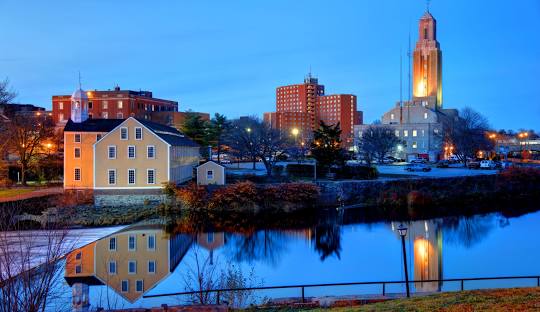 View of Pawtucket's cityscape at dusk, featuring illuminated buildings and their reflections in a calm body of water, where local businesses thrive with the help of managed IT services.