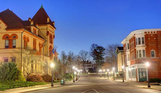 A quiet street at twilight with illuminated lampposts, a historic building on the left, and a brick building on the right, leads to a tree-lined residential area where managed IT services in Westerly have made their mark.
