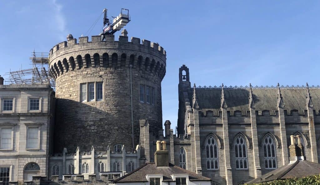 Stone tower connected to a detailed, Gothic-style building with arched windows under a clear blue sky. A construction crane and scaffolding are visible near the tower's top, reminiscent of the meticulous planning seen in Managed IT Services Dublin Ireland.