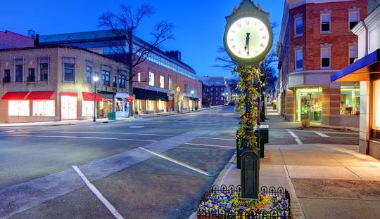 A street scene in Greenwich, CT, featuring an old-fashioned clock on a post adorned with flowers. The street is lined with buildings and appears calm and quiet in the evening, much like the seamless efficiency of managed IT services in this serene setting.