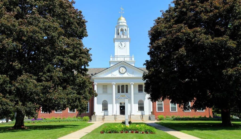 Front view of a large brick and white clock tower building with columns at the entrance, flanked by two large trees and a well-maintained lawn, perfectly embodying the charm of Stratford CT where managed IT services ensure seamless operations.