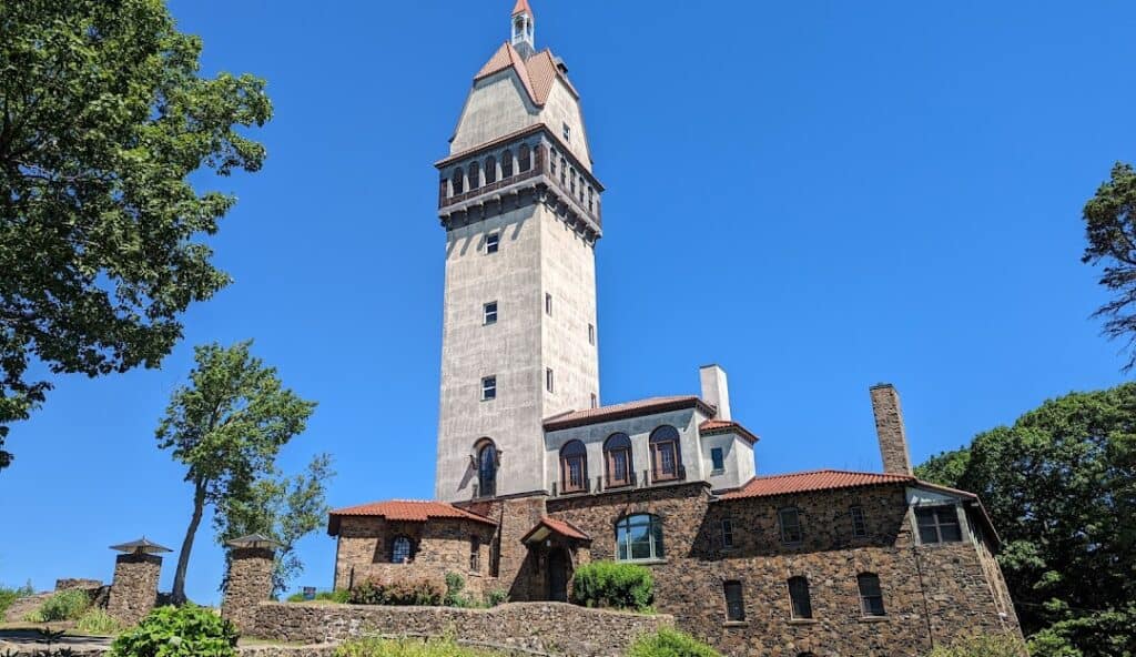 A tall stone and brick tower with a clock on top stands proud, surrounded by trees under a clear blue sky, much like the reliable managed IT services Windsor CT relies on.