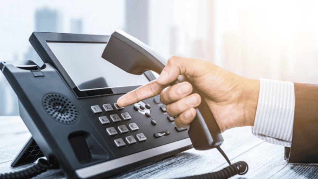 A hand holding a office telephone receiver, positioned above the keypad.