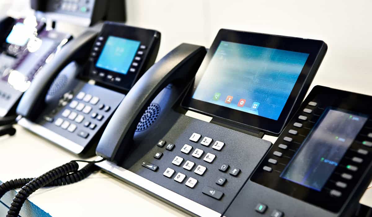 Row of modern office desk phones with touchscreens and keypads.