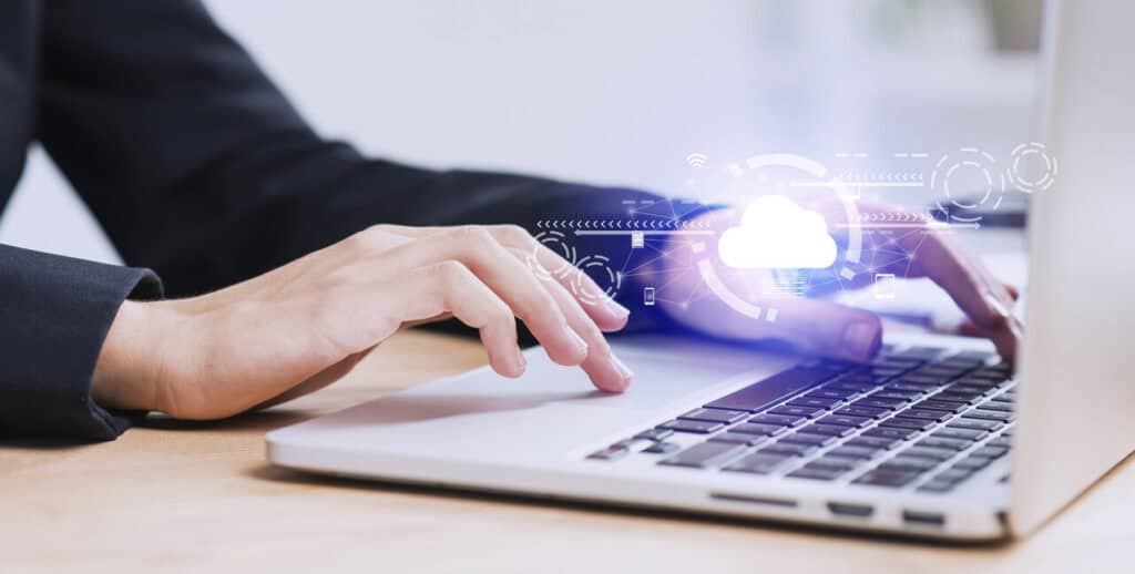 Hands typing on a laptop keyboard, with a digital cloud icon and network symbols hovering over the keys, illustrating the cost savings potential of cloud computing.