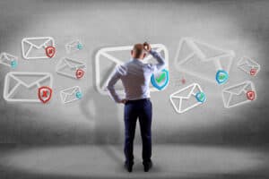 A man stands scratching his head, facing floating icons of email envelopes—some with check marks, others with red Xs—highlighting email authentication for business and the need to prevent email spoofing.