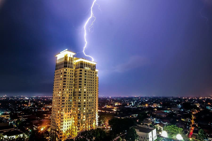 A lightning bolt strikes the roof of a tall, illuminated building at night, city lights shining below—an electrifying reminder of the importance of strong ransomware protection for small business.