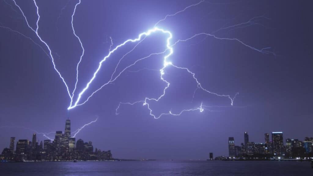 Bright lightning bolts strike a tall building in a city skyline at night, illuminating the sky above water—reminiscent of the power and reliability cloud servers for small business can offer.