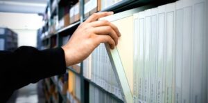 A person’s hand pulls a file folder from a row of organized files on a shelf in an office, following IRS Publication 4557 guidelines for safeguarding taxpayer data.