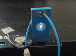 Close-up of two security keys connected to a device for cyber security and network firewall protection—one YubiKey with illuminated “y” symbol in USB port, and one blue key attached to a cable—demonstrating data security, endpoint security, cloud security, information security, IT support, and compliance solutions for small and medium businesses.