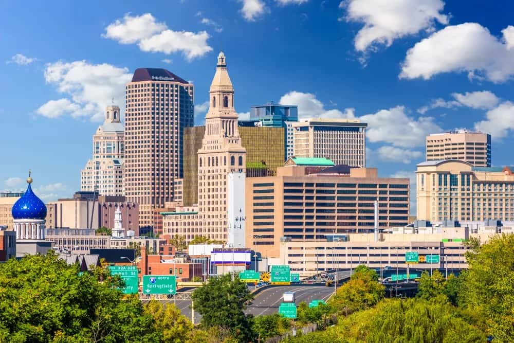 Downtown city skyline with modern and historic buildings, highway signs, trees, and blue sky—ideal for cyber security, network firewall, and data security themes.