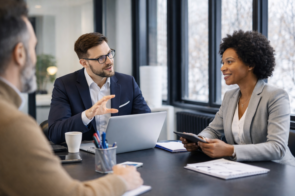 Three business professionals discuss cyber security, network firewall, data compliance, and cloud security at a modern office table.
