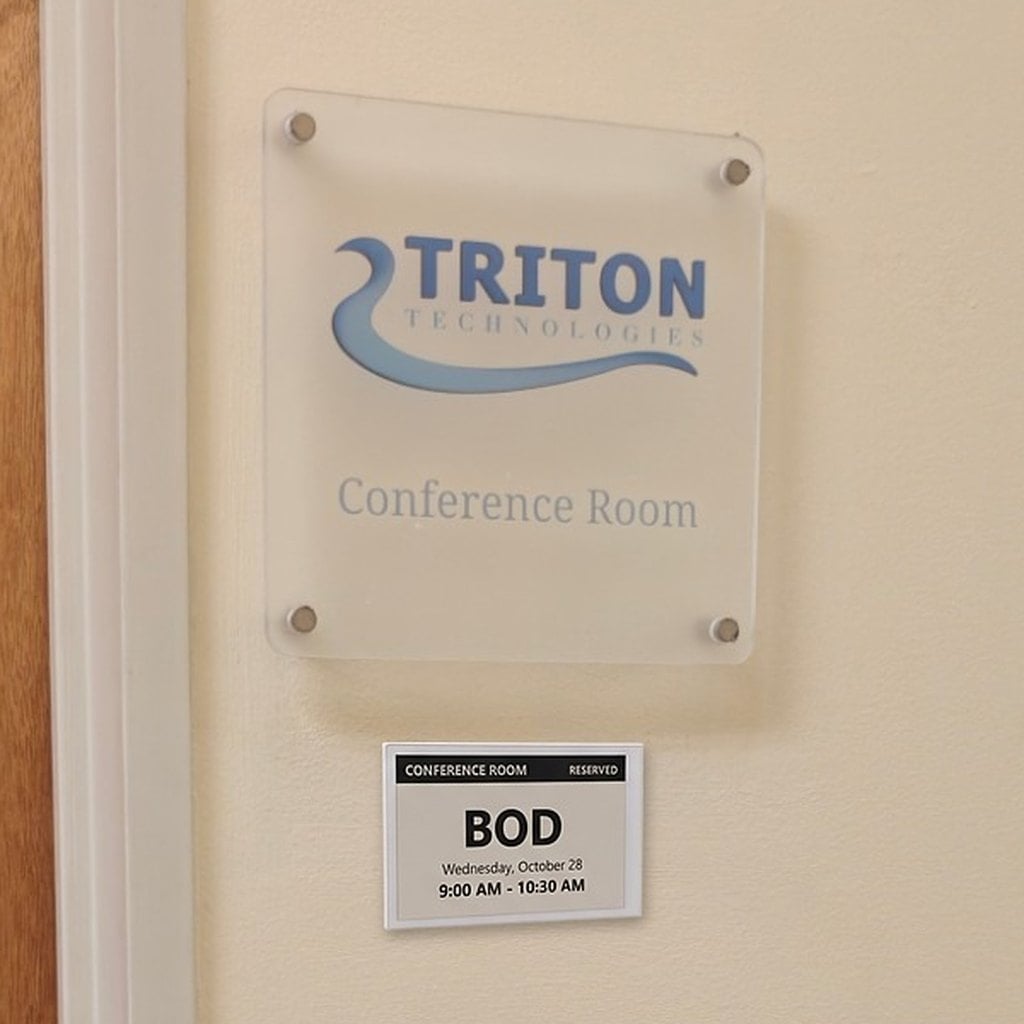 E-ink conference room door sign below a Triton Technologies plaque, showing a BOD meeting reserved Wednesday 9:00 to 10:30 AM