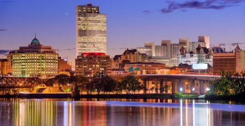 Twilight cityscape with illuminated buildings reflected on a calm river, showcasing the glow of managed IT services in Albany.