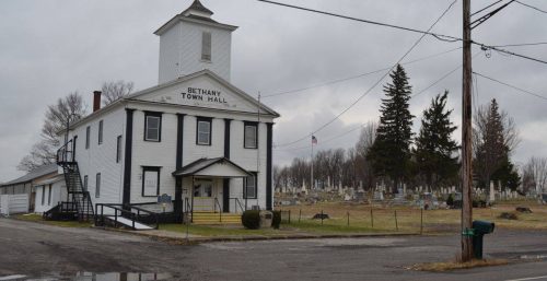 Bethany town hall building, managed by IT services in Bethany, is adjacent to a cemetery on an overcast day.