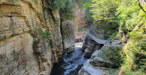 A narrow river flows through a rocky canyon with steep cliffs. A stone path with railings runs along the right side, and a few people are walking on it. Dense greenery surrounds the area, creating a serene backdrop reminiscent of managed IT services Chesterfield’s streamlined efficiency in nature.