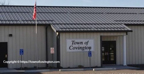 A beige metal building with a sign reading "Town of Covington" above the entrance. An American flag flies on a pole nearby, proudly waving above two handicapped parking signs. Close to the heart of managed IT services in Covington, this spot is both welcoming and community-focused.