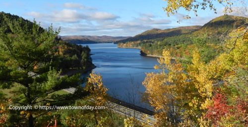 A scenic view of a reservoir surrounded by autumn foliage, hills, and a partly cloudy sky. A road runs along the shore at the bottom of the image, reminiscent of the tranquility one might find while exploring areas around Preston, even while searching for managed IT services.