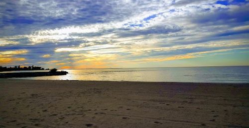 A tranquil beach scene at sunset with a cloudy sky, calm sea, and sand in the foreground, reminiscent of the serene environment found in Fair Haven. Shadows of land are visible to the left horizon, where managed IT services ensure smooth operations behind the scenes.