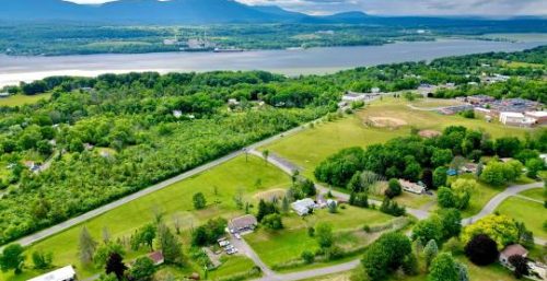 Aerial view of a rural landscape with scattered houses, green fields, trees, and a river in the background with mountains on the horizon under a cloudy sky—a serene setting that belies the bustling managed IT services in Germantown.