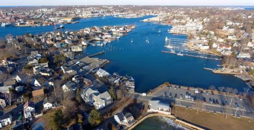Aerial view of a coastal town managed by IT services in Gloucester, with a road running parallel to a waterway, dotted with boats and surrounded by residential neighborhoods.