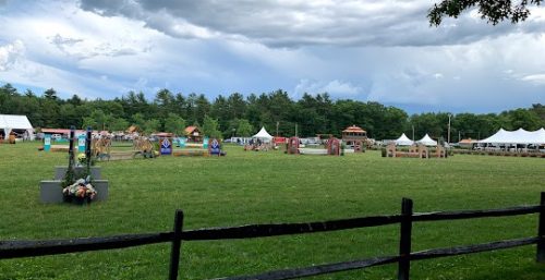 Outdoor event with multiple white tents and colorful booths, managed by IT service from Halifax, set up in a grassy field enclosed by a wooden fence under a cloudy sky.
