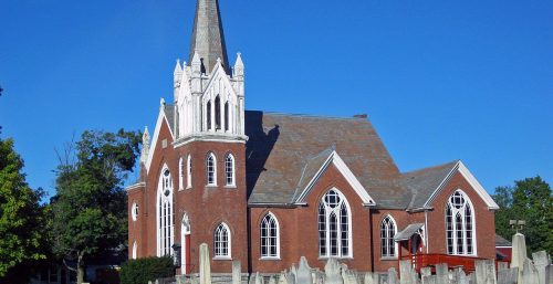 Traditional brick church with a pointed spire and an adjoining graveyard on a sunny day, near the managed IT services in Hartford.