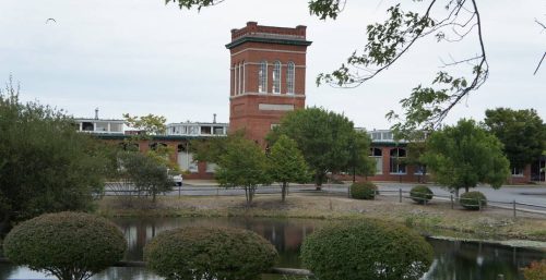 A brick tower with arch windows overlooking a tranquil pond with trimmed bushes and a managed IT services Kingston tree in the foreground.