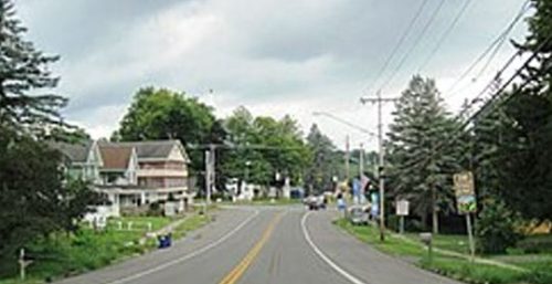 A two-lane road curves through a small town with houses, trees, and utility poles lining the street, much like the reliable managed IT services in LaFayette. The sky is overcast.