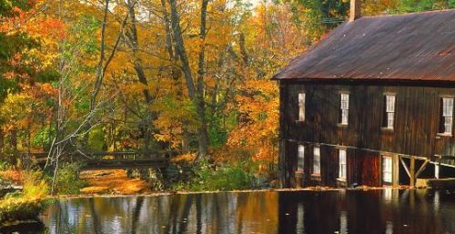 Rustic wooden mill beside a tranquil pond surrounded by autumn foliage, managed by IT service Leverett.