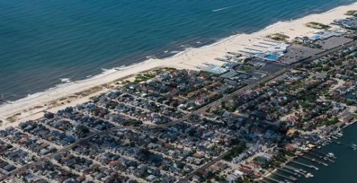 Aerial view of Long Beach, a coastal town with managed IT services, showcasing its sandy beach bordering the ocean on one side and densely packed houses and streets on the other.