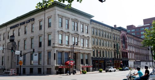 Classic architecture buildings in a city street with a motorcyclist waiting at a traffic light near the "Managed IT Services Louisville" office.