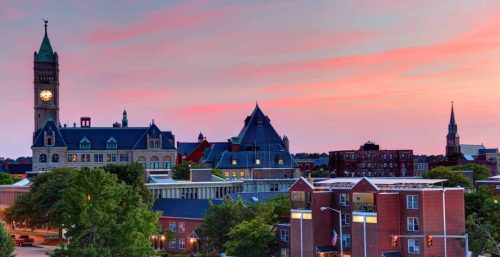 Historic buildings with a clock tower managed by IT services Lowell stand out against a pink and blue sunset sky in a cityscape.