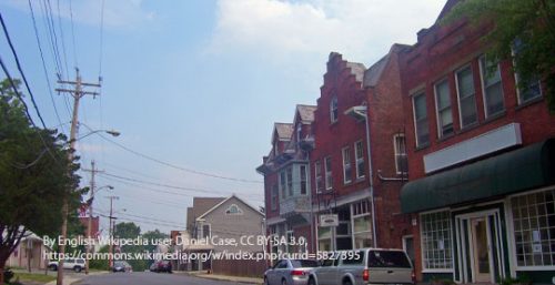 A small town street in Milton with red brick buildings, parked cars, and power lines. The sky is partly cloudy. Perhaps one of the businesses offers managed IT services to keep the community connected.