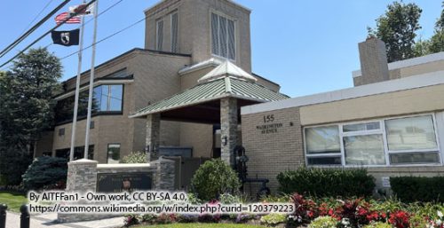 A two-story building with a brick façade, identified as Washington Avenue, houses managed IT services in Mineola. A flagpole with a flag stands in front, and there are shrubs along the sidewalk.