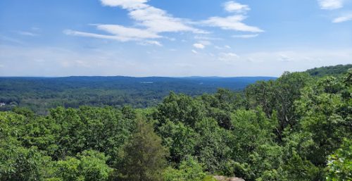 A scenic view of a vast forested landscape under a partly cloudy blue sky. The dense green trees stretch toward the horizon, blending into the distant hills. It's as serene as the reliable managed IT services you can find in Montebello.