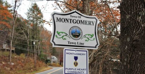 Two signs by the roadside: one indicating the town line for the Town of Montgomery and the other noting Montgomery as a Purple Heart Community, set against a backdrop of trees and autumn foliage. It's clear that managed IT services thrive in this community-focused environment.