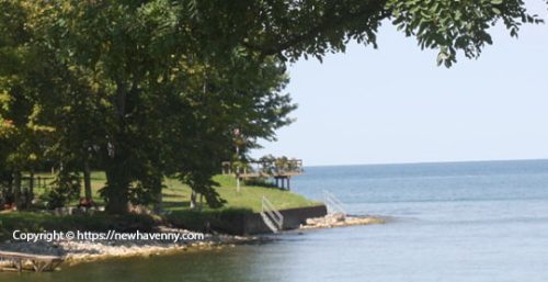 Calm lakeside view with large green trees, a small pier, steps leading into the water, and just beyond, the town known for its managed IT services—New Haven.