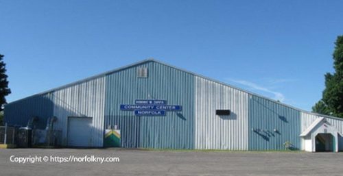 A large, blue metal building with a sign reading "Community Center Norfolk" stands prominently. Managed IT services in Norfolk ensure the facility's tech runs smoothly. Multiple windows and doors mark its facade, set against a clear sky backdrop.