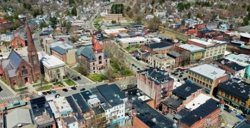 Aerial view of a small town with a mix of old and modern buildings, featuring a prominent church on the left and a clock tower in the center. Streets, houses, and businesses offering managed IT services in Northampton are visible in the background.